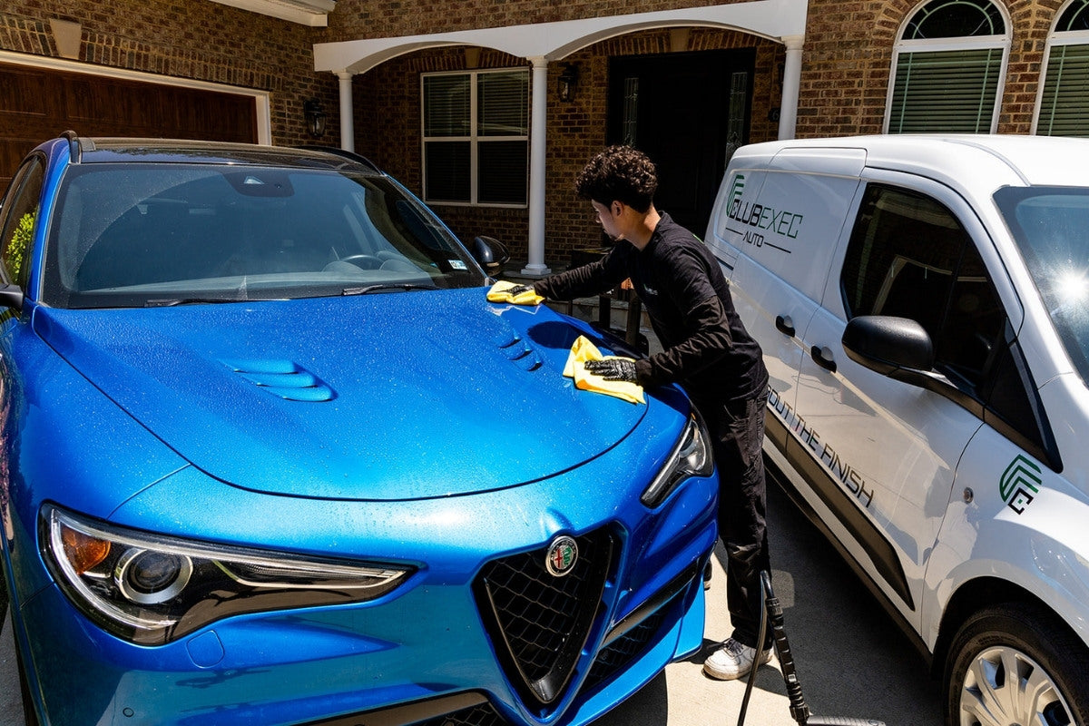 Person cleaning a blue car with a white van in the background