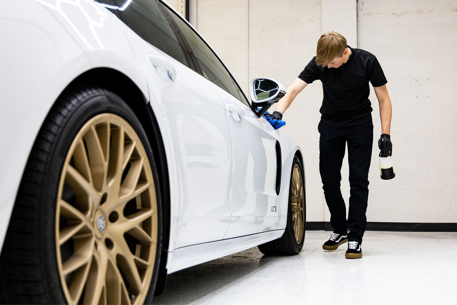 Person cleaning a white car with gold rims in a garage.