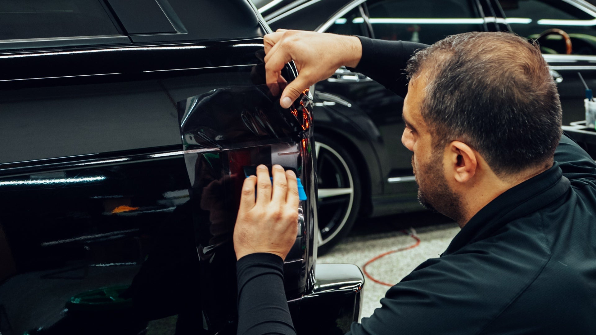 Person working on a car's exterior with tools in a garage setting